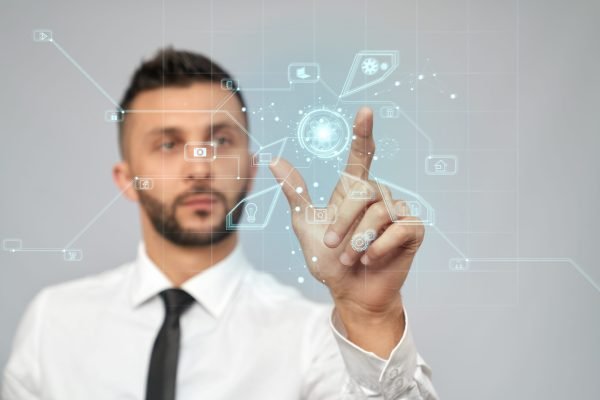 Front view of young serious businessman in formal suit in office. Selective focus of digital tactile charts screen, bearded man clicking virtual icon. Concept of high technologies, digitalization.